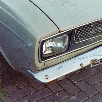 The image features a vintage car parked on the side of a brick road. The car is an old model, possibly a Ford, and it appears to be in need of repair or restoration. It has a dented hood and a missing bumper, giving it a worn-out appearance.