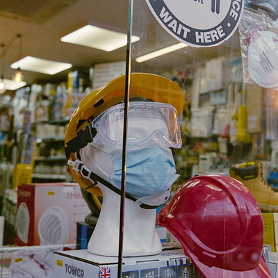 The image features a store display with various items on sale. There are two safety helmets, one red and the other yellow, placed in front of a window. A sign is visible above them, possibly indicating their purpose or price.