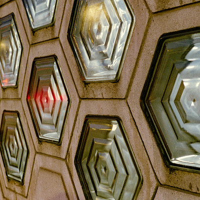 The image features a wall with a unique design made up of many small hexagonal shapes. These hexagons are arranged in a pattern, creating an interesting visual effect. Each hexagon is covered with a glass-like material that reflects light and adds depth to the overall appearance.