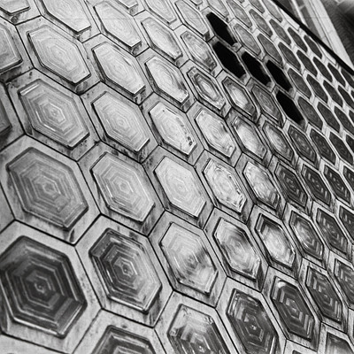 The image features a large, intricate tile design with many small hexagonal shapes. These tiles are arranged in a pattern that creates an interesting and visually appealing surface. The tiles are made of metal, giving them a shiny appearance.
