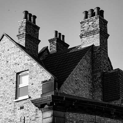 The image features a large brick house with two chimneys on top. The house has a black and white color scheme, giving it an old-fashioned appearance. There are four windows visible in the scene, one on each side of the house.
