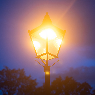 The image features a street light with two lights on it, one at the top and another at the bottom. The light is shining brightly in the dark night sky, illuminating the area around it. There are trees visible in the background, adding to the overall atmosphere of the scene.