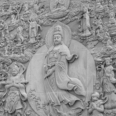 The image features a beautifully carved statue of Buddha, surrounded by intricate designs and other statues. The main statue is positioned in the center of the scene, with various other figures surrounding it on all sides. Some of these figures are located near the top, while others can be seen at different heights throughout the image.