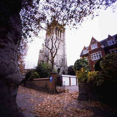The image features a large brick building with a clock tower, which appears to be an old church. The building is surrounded by trees and has a fence in front of it. There are several windows on the building, some of which have curtains drawn over them.