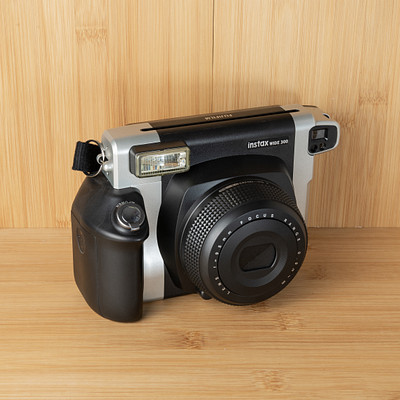 The image features a silver and black camera sitting on top of a wooden table. The camera is positioned in the center of the scene, with its lens facing upwards. The table appears to be made of wood, giving it a warm and natural appearance.