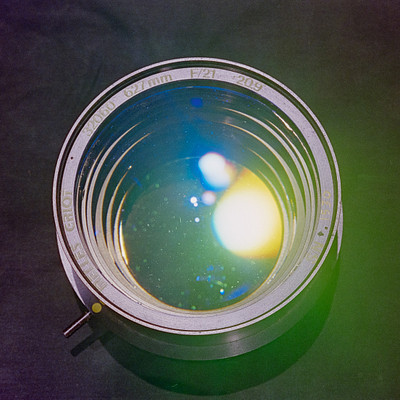 The image features a silver metal object with a glass lens, which appears to be an old-fashioned camera. It is placed on a table or countertop, and the lens has a blue tint to it. There are two small circles of light visible through the lens, creating a unique visual effect.