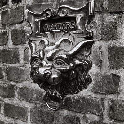 The image features a brick wall with a metal mailbox attached to it. The mailbox has an interesting design, resembling a dragon or a lion head. It is situated on the side of the brick wall and appears to be a unique addition to the building's exterior.