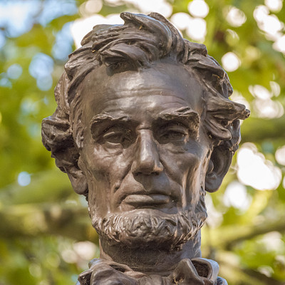 The image features a statue of Abraham Lincoln, the 16th President of the United States. The statue is made of metal and has a bronze finish, giving it an antique appearance. It captures the essence of the historical figure with its detailed facial features and posture.