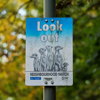 The image features a blue and white sign on a pole, which is placed in front of some trees. The sign has an alien theme with five different aliens depicted on it. These aliens are positioned at various heights and angles, creating a visually interesting scene.