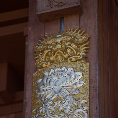 The image features a wooden structure with an ornate design on the wall. There is a gold and silver decoration, possibly a piece of art or a symbol, attached to the wood. The decoration has a sun-like shape in its center, surrounded by intricate patterns and designs.