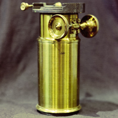 The image features a large, old-fashioned brass object with a gold color. It appears to be an antique or vintage item, possibly used for measuring or other purposes. The object is placed on a black background, which helps emphasize its unique appearance and texture.