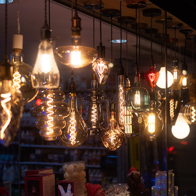 The image features a store with an abundance of light bulbs hanging from the ceiling. There are numerous glass globes and lights, creating a visually appealing display. Some of these lights have a yellowish tint to them, adding warmth to the scene.