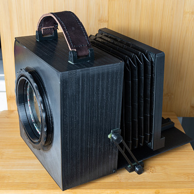 The image features a black camera with a brown leather strap attached to it. It is placed on top of a wooden table, which serves as the background for this scene. The camera appears to be an old-fashioned model, possibly made from wood or other materials that give it a vintage appearance.