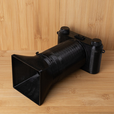 The image features a black camera with a large lens, sitting on top of a wooden table. The camera is positioned in such a way that it appears to be pointing upwards or towards the ceiling. The wooden surface beneath the camera adds an interesting contrast to the modern design of the device.