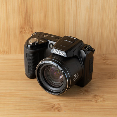 The image features a black Nikon camera sitting on top of a wooden table. The camera is placed in the center of the scene, with its lens facing upwards. The wooden surface provides an appealing backdrop for this photography equipment.