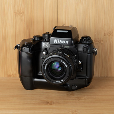 The image features a black Nikon camera sitting on top of a wooden table. The camera is placed in the center of the scene, with its lens facing forward. The wooden surface provides an appealing backdrop for this classic photography equipment.