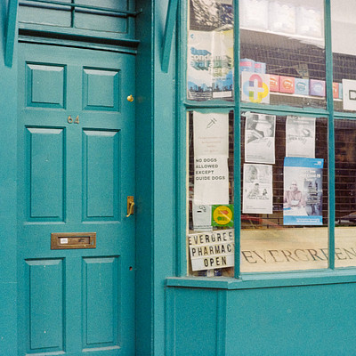 The image features a green door with a sign on it, indicating that the building is open. Inside the building, there are several signs posted on the wall and a window visible in the background. A car can be seen parked outside of the building, adding to the overall atmosphere of the scene.