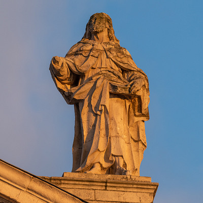 The image features a statue of Jesus, possibly made of stone or concrete, standing on top of a building. The statue is positioned in the middle of the scene and appears to be looking upwards towards the sky. The statue's face is visible, giving it an impressive presence as it overlooks its surroundings.