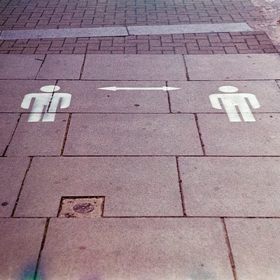 The image is a black and white photo of a sidewalk with two men's silhouettes painted on the ground. These silhouettes are used to indicate the direction of the crosswalk, which is located at an intersection. The sidewalk appears to be made of brick or stone, giving it a classic appearance.