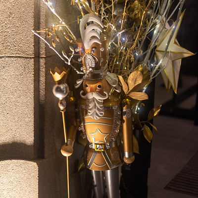 The image features a statue of a man dressed in medieval armor, standing next to a wall. He is holding a staff and appears to be wearing a crown on his head. The statue has a unique appearance with gold accents and decorations, making it stand out from the surroundings.