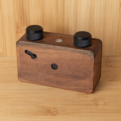 The image features a wooden camera with two black knobs on the top. It is placed on a table, possibly made of wood as well. The camera appears to be an old-fashioned model, adding a vintage touch to its design.