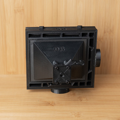 The image is a close-up of an old, black camera with a wooden background. The camera has a lens on the front and appears to be in good condition despite its age. It seems to be a vintage item that may have been used for photography or other purposes in the past.