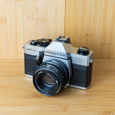 The image features a silver and black camera sitting on top of a wooden table. The camera is an old-fashioned model, possibly a vintage or antique item. It appears to be well-maintained and ready for use.