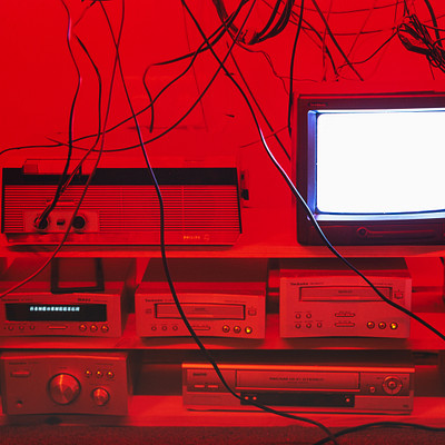 The image features a television set sitting on top of an entertainment center. The TV is positioned in the middle of the scene, surrounded by various electronic devices and equipment. There are two VCRs placed next to each other, with one located closer to the left side of the TV and the other towards the right.