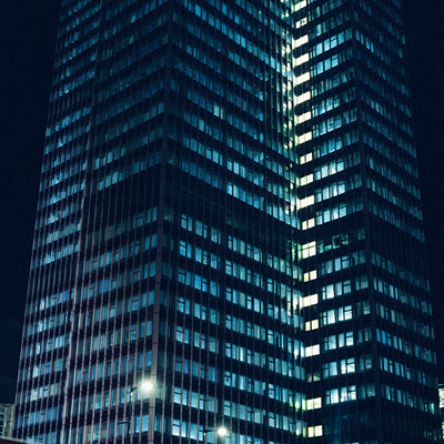 The image features a tall, dark building with many windows. It appears to be an office building or a similar type of structure. The building is lit up at night, creating a striking contrast against the darkness of the sky.