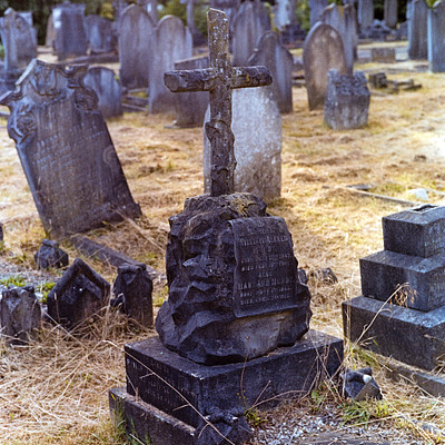The image features a cemetery with numerous headstones and crosses. A prominent black stone cross stands out in the foreground, surrounded by other gravestones. Some of these stones are placed on the grass, while others are situated closer to the ground.
