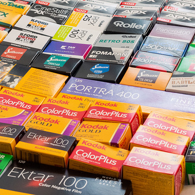 The image features a large collection of various film and camera batteries. There are numerous packages of different sizes, colors, and brands displayed on the table. Some of these packages include batteries for Canon cameras, while others have batteries for other types of cameras.
