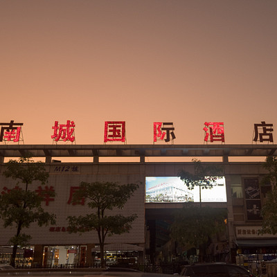 The image features a large building with an Asian-style sign on top of it. The sign is written in Chinese and appears to be lit up, making it stand out against the dark sky. There are several cars parked outside the building, including one near the left side, another further back, and two more towards the right side.