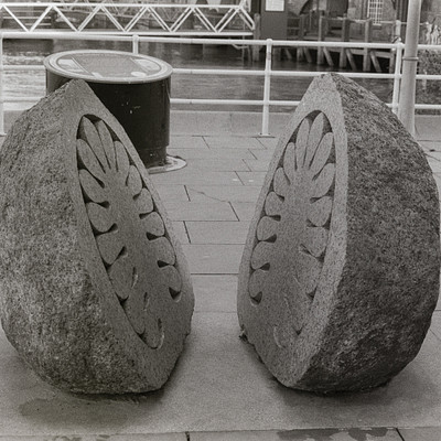 The image features two large, decorative stone sculptures sitting on a sidewalk. These unique pieces of art are placed next to each other and appear to be made from concrete or similar materials. They have intricate designs on them, adding an interesting visual element to the scene.