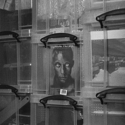 The image is a black and white photo of a man's face, which appears to be a sticker or a picture on the side of a plastic container. There are several other containers in the background, some of them stacked up against each other. The overall scene gives an impression of a storage area with various items stored inside the containers.