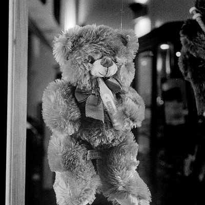 The image is a black and white photo of a teddy bear hanging from the ceiling. It appears to be a decoration or a unique way of displaying the stuffed animal. The teddy bear has a bow around its neck, adding an extra touch of charm to the scene.