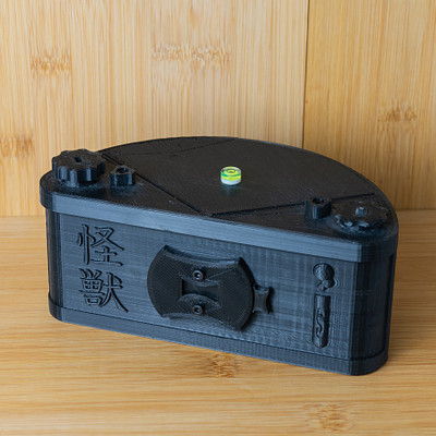 The image features a small black box with an Asian design on it. Inside the box, there is a green light that appears to be lit up. The box has a handle and is placed on top of a wooden table.