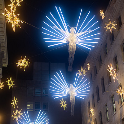 The image features a city street at night, illuminated by numerous lights. There are several large white stars hanging from the ceiling, creating an impressive display. In addition to these stars, there is a group of angel-like figures suspended in mid-air, adding to the festive atmosphere.
