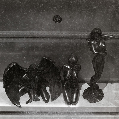 The image is a black and white photo of three statues, each depicting a different angel. They are arranged in a row on a table or countertop. The first statue is positioned to the left, the second one is in the middle, and the third one is on the right side.