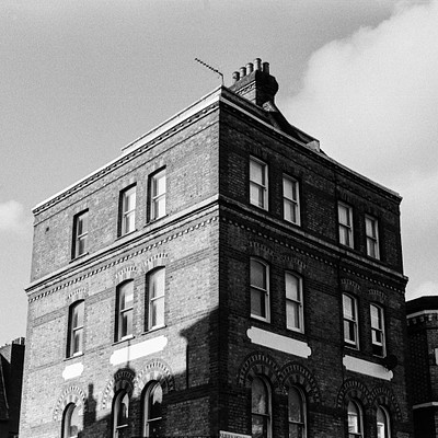 The image is a black and white photo of an old brick building with many windows. The building has a clock tower on top, giving it a classic appearance. There are several windows visible in the scene, some located near the top of the building while others can be seen at various heights throughout the structure.