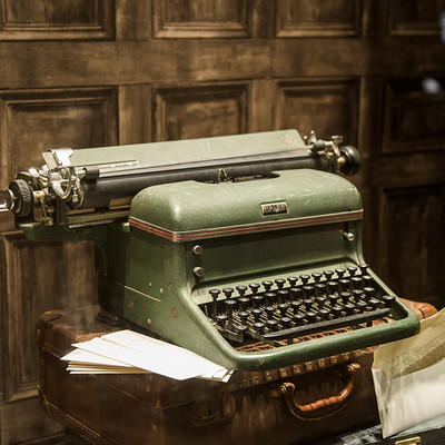 The image features a vintage green typewriter sitting on top of a wooden desk. The typewriter is an old-fashioned model, and it appears to be in good condition. There are several papers scattered around the typewriter, indicating that it has been used recently or is ready for use.