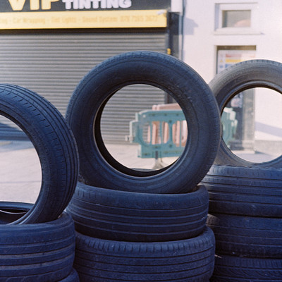 The image features a large pile of tires stacked on top of each other, with some of them being black and others white. These tires are placed in front of a building that has the name "VIP Window Tinting" written on it. There is also a car visible in the background, adding to the overall scene.