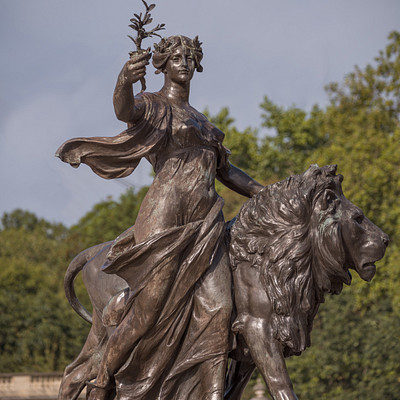 The image features a statue of a woman riding on the back of a lion. She is holding a crown in her hand, and the statue appears to be made of bronze. The woman's outfit suggests that she might be depicted as a goddess or a mythical figure.
