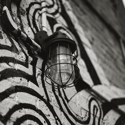 The image is a black and white photo of an outdoor wall with a light fixture attached to it. The light fixture has a glass globe, which adds a unique touch to the overall design. The wall appears to be covered in graffiti or artwork, giving it a distinctive appearance.