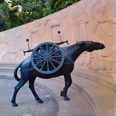 The image features a large metal sculpture of a horse pulling a cart. The horse is positioned in the center of the scene, and the cart appears to be an old-fashioned wagon with wooden wheels. The horse statue has a unique design, giving it a distinctive appearance.