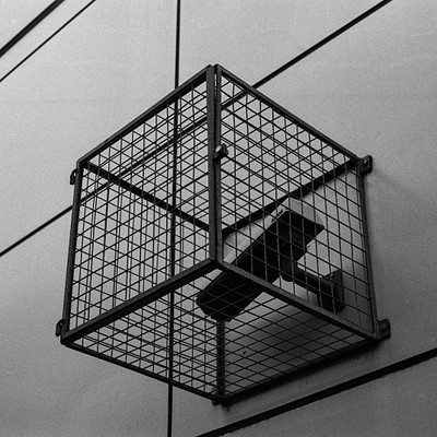 The image features a small cage with a camera inside of it. The cage is attached to the wall, and the camera appears to be capturing an interesting perspective from within the enclosure. The cage itself has a metal structure, giving it a unique appearance.