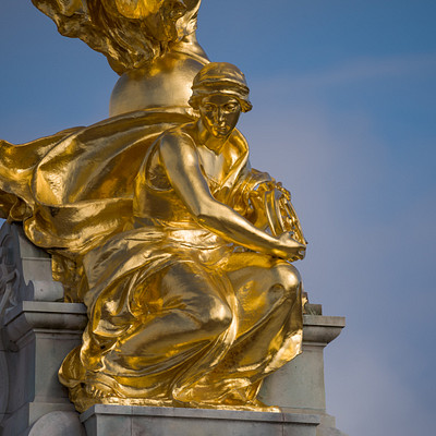 The image features a statue of an angel sitting on top of a pedestal. The statue is made of gold and has intricate details, making it appear quite ornate. The angel appears to be holding a book in its hands, adding to the artistic nature of the sculpture.