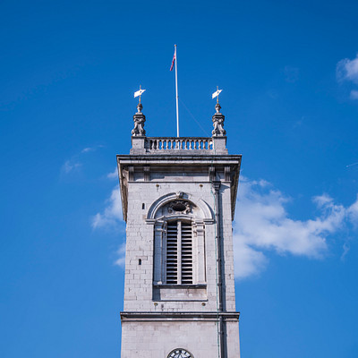 The image features a large, tall clock tower with a steeple and a cross on top. The clock is prominently displayed on the side of the building, making it easily visible to passersby. The sky in the background is blue, creating a beautiful contrast against the white structure of the tower.