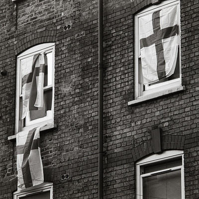 The image is a black and white photo of an old brick building with two windows. Each window has a flag hanging from it, adding a unique touch to the scene. The flags are positioned in such a way that they appear to be waving in the wind, giving the impression of movement.