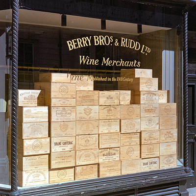 The image features a storefront with a large display of wine boxes. There are several stacks of wine boxes, some on the ground and others on shelves, creating an eye-catching presentation for passersby. The store appears to be selling wine merchandise, as indicated by the sign above the window.