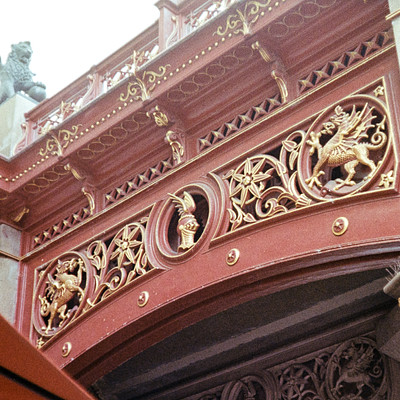 The image features a red and gold decorative structure with intricate carvings. This ornate piece of art is likely an architectural feature, such as a balcony or a part of a building's facade. The design includes various figures and patterns that add to the overall beauty of the structure.